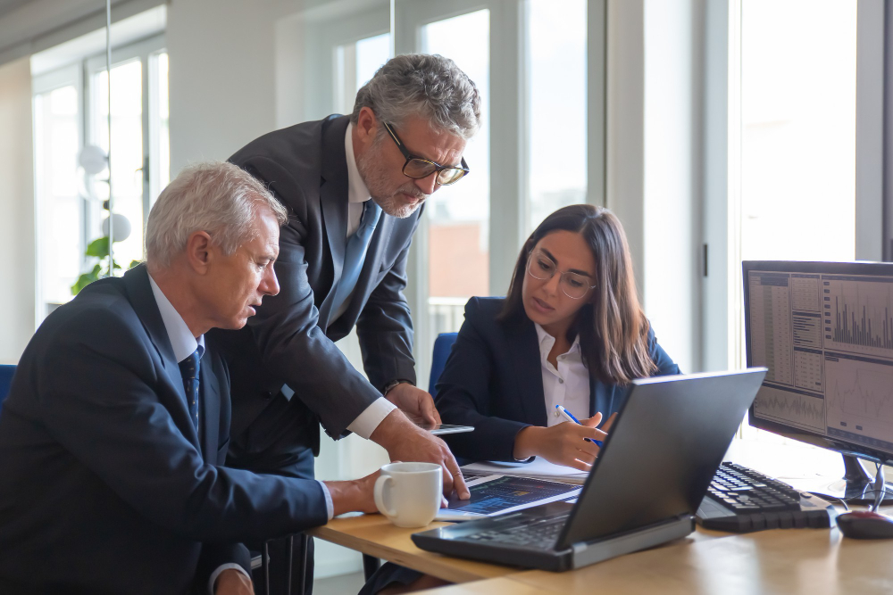 Business leaders collaborating around a laptop in an office setting, symbolizing Extend Your Team’s expertise in creating smarter teams.